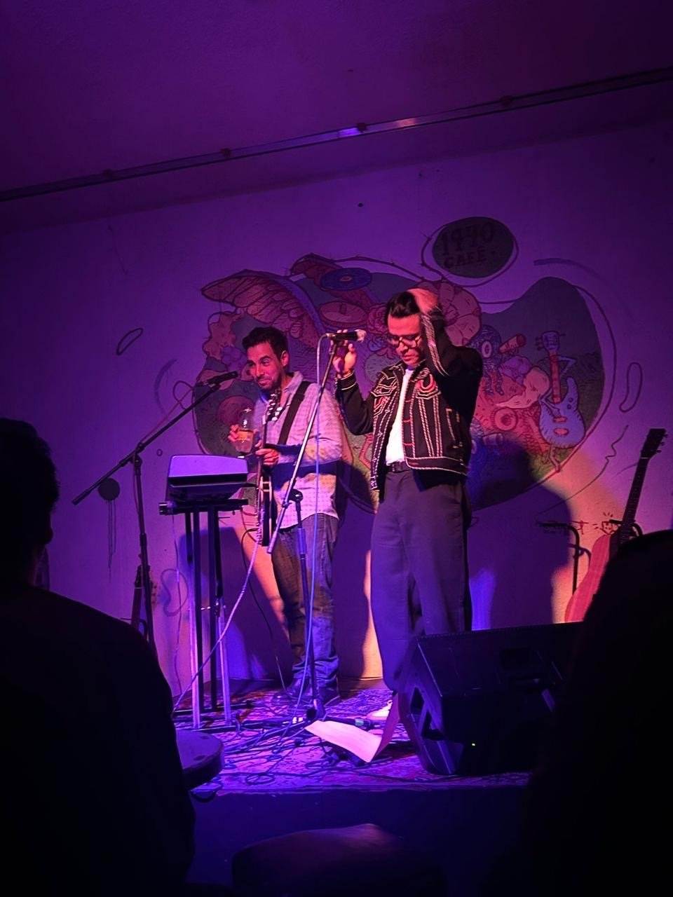 Hombres cantando y tocando una guitarra en un escenario pequeño.