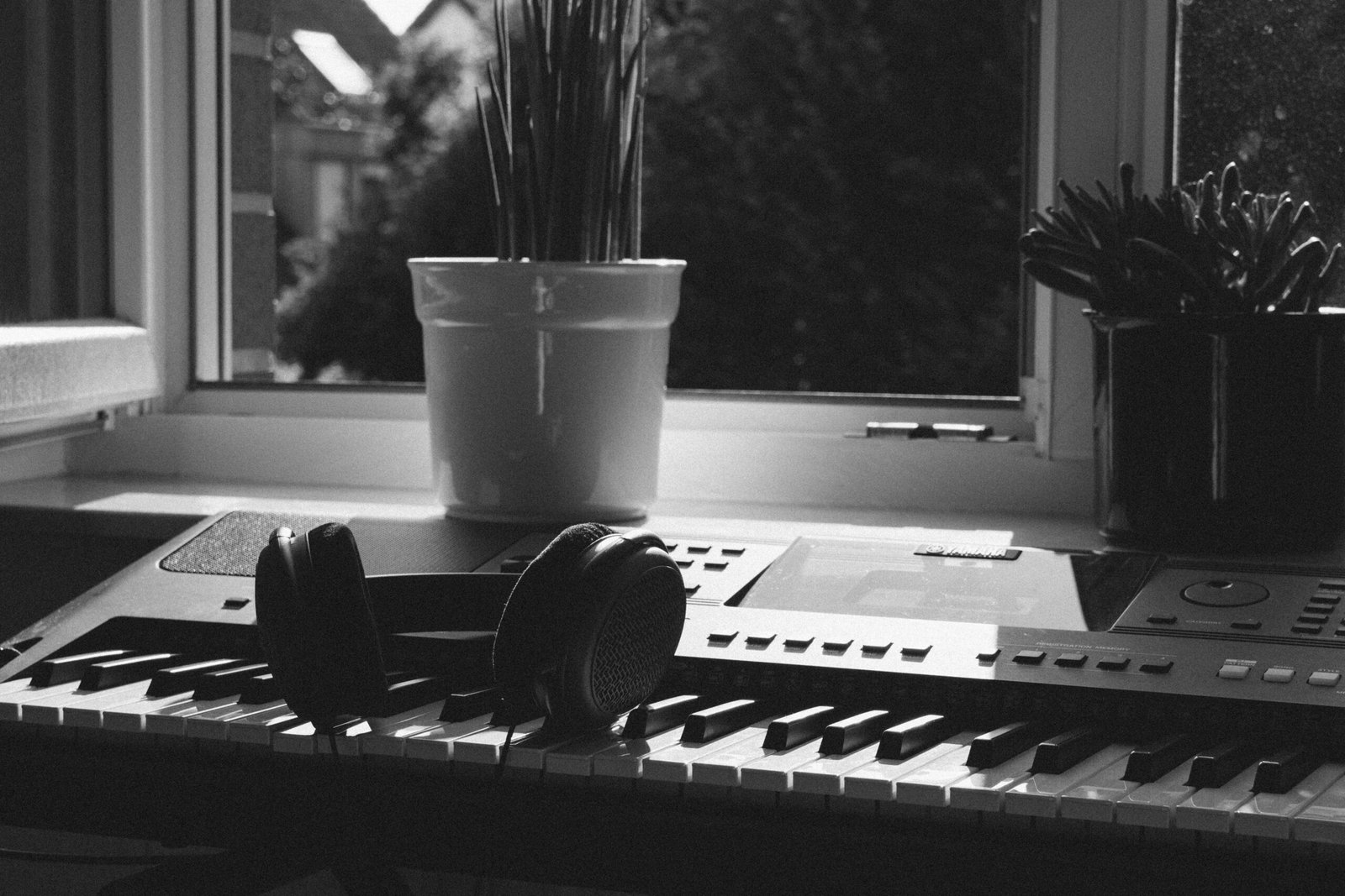 Teclado musical con audífonos sobre las teclas, junto a una ventana con luz natural.