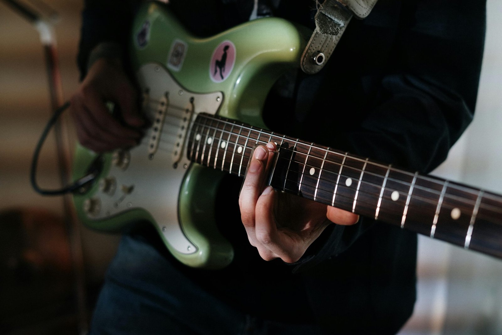 Manos tocando guitarra eléctrica verde en primer plano