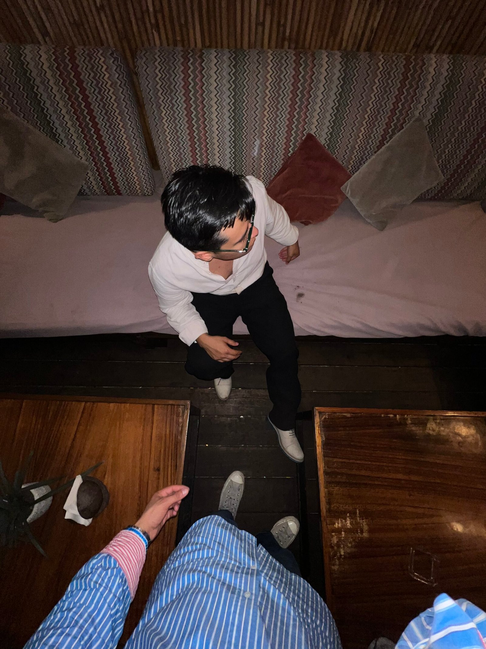 Lanzamientos Hombre vista desde arriba de una persona de pie junto a una sala de estar en una habitación. al frente, una persona de lentes con pantalón negro y camisa blanca, viendo a un lado.