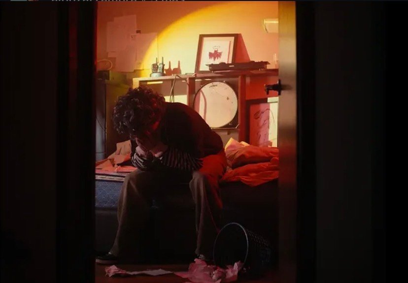 Sencillos Hombre sentado en habitación con iluminación cálida y ambiente introspectivo.